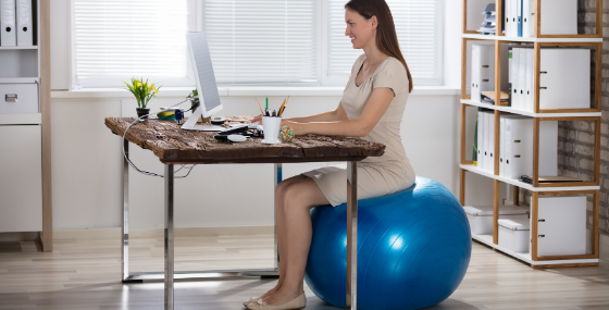 woman sitting on exercise ball at work - 5 Ways To Be Healthier At Work Every Day