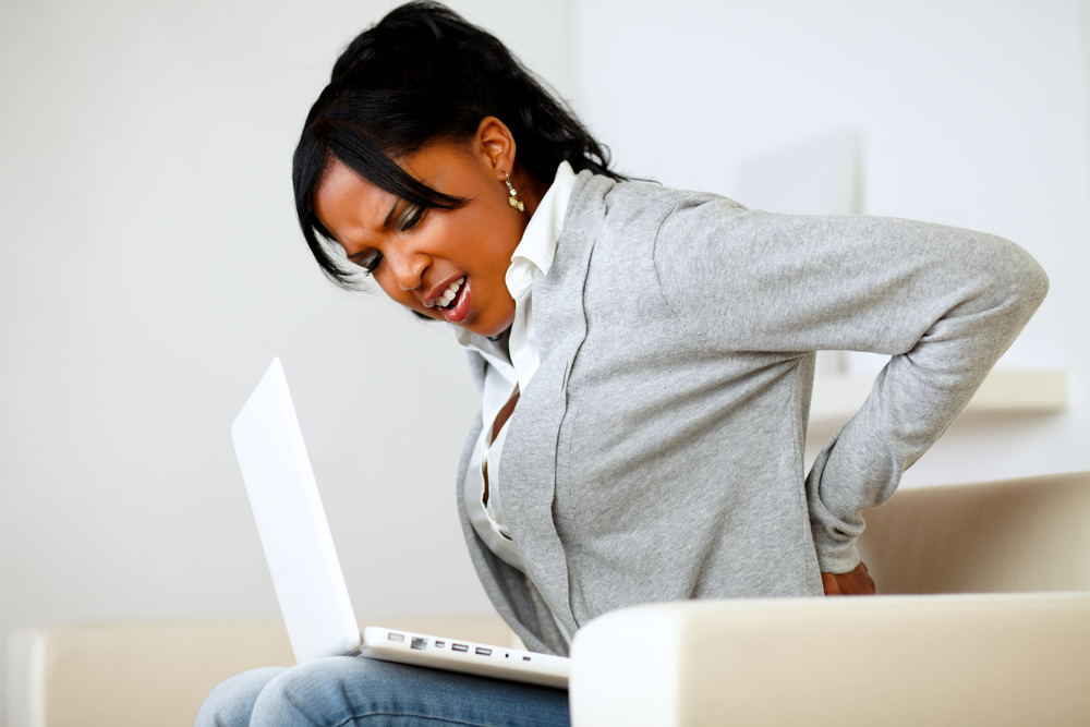 woman of color sitting with back pain. How To Prevent And Relieve Back Pain