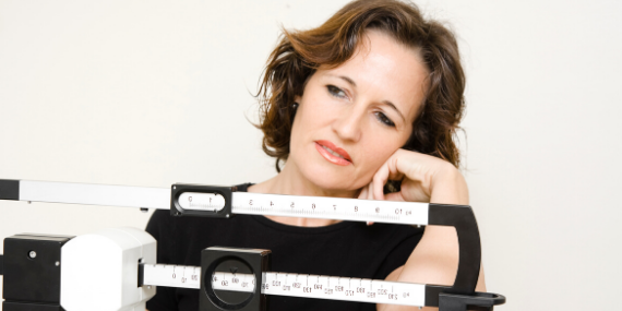 Woman frowning at scale - What you can do if you’re struggling to lose weight - heike yates