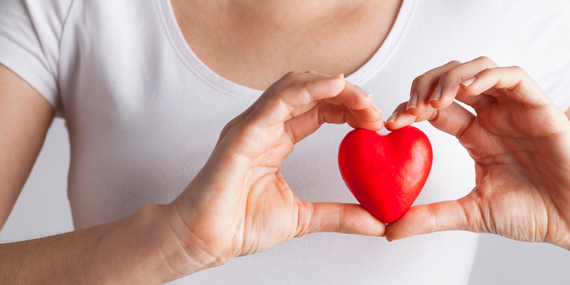 woman in white t-shirt holding a red heart over her heart 5 Ways To Improve Heart Health For Women Over 50 