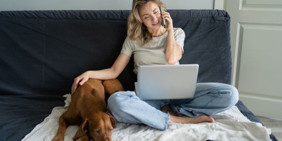 woman sitting on the couch with laptop, phone and dog