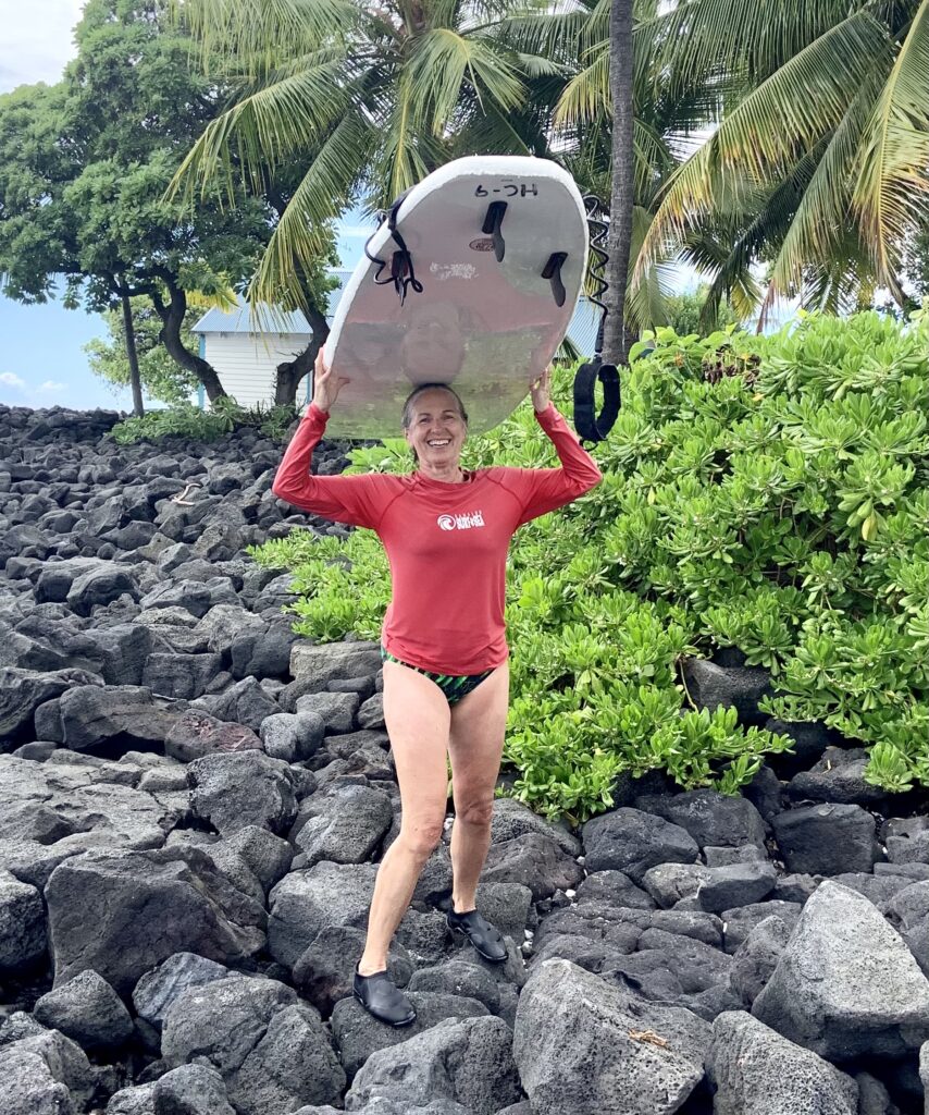 Heike Yates smiling with surfboard – midlife confidence and joy
