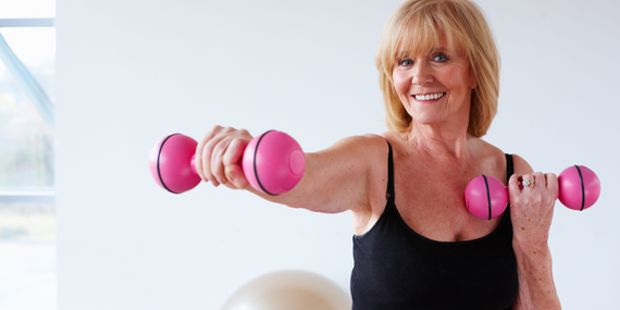 Woman smiling into the camera and pushing pink weights to prevent weight gain in midlife