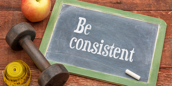 Staying Consistent in Midlife: Why Old Habits Stop Working—and What to Do Instead, a sign saying be consistent with weights and an apple